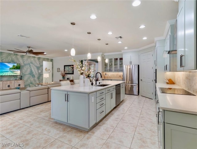 kitchen with pendant lighting, backsplash, a center island with sink, sink, and appliances with stainless steel finishes