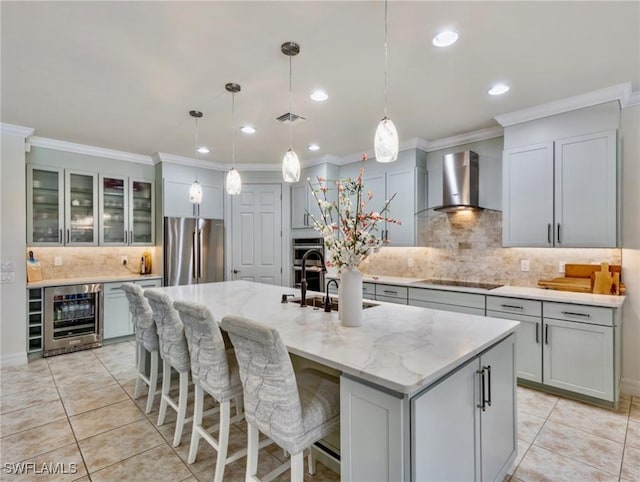 kitchen featuring wall chimney exhaust hood, wine cooler, decorative light fixtures, a kitchen island with sink, and appliances with stainless steel finishes