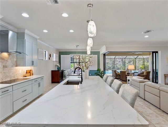 kitchen featuring wall chimney exhaust hood, light stone counters, sink, and hanging light fixtures