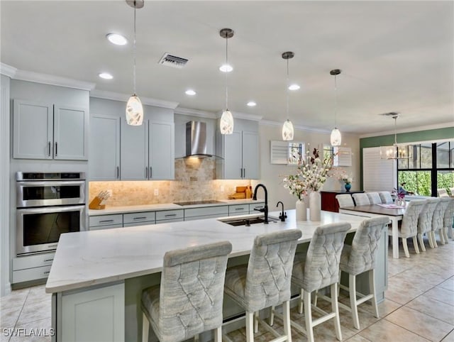 kitchen with a large island, sink, light stone countertops, wall chimney range hood, and black electric stovetop