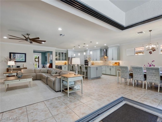 tiled living room with ceiling fan with notable chandelier and ornamental molding