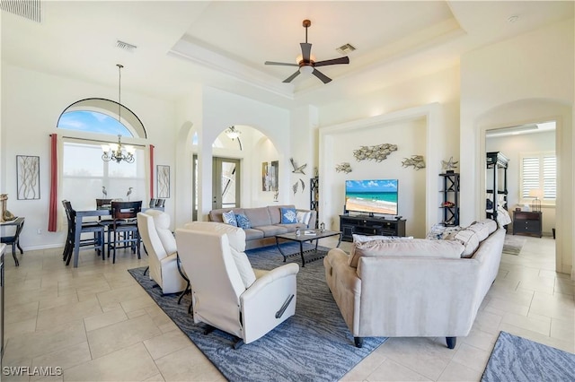 tiled living room featuring a raised ceiling, a towering ceiling, a healthy amount of sunlight, and ceiling fan with notable chandelier