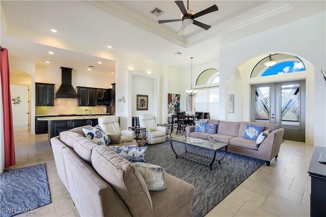 living room with a tray ceiling, french doors, light tile patterned floors, and ceiling fan with notable chandelier