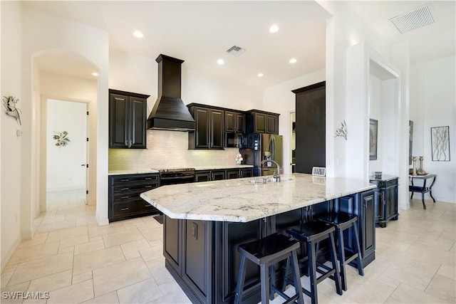 kitchen with sink, light stone counters, premium range hood, a breakfast bar area, and decorative backsplash