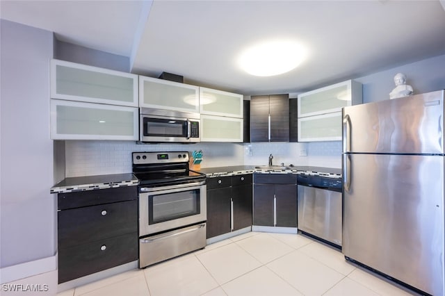 kitchen with glass insert cabinets, appliances with stainless steel finishes, decorative backsplash, and a sink