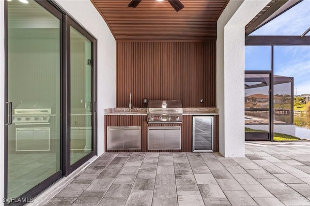 view of patio with grilling area, ceiling fan, beverage cooler, glass enclosure, and an outdoor kitchen