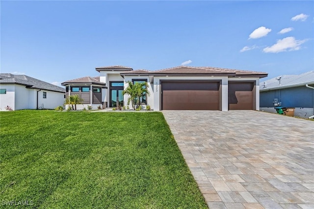 prairie-style home with a garage, decorative driveway, a front lawn, and stucco siding