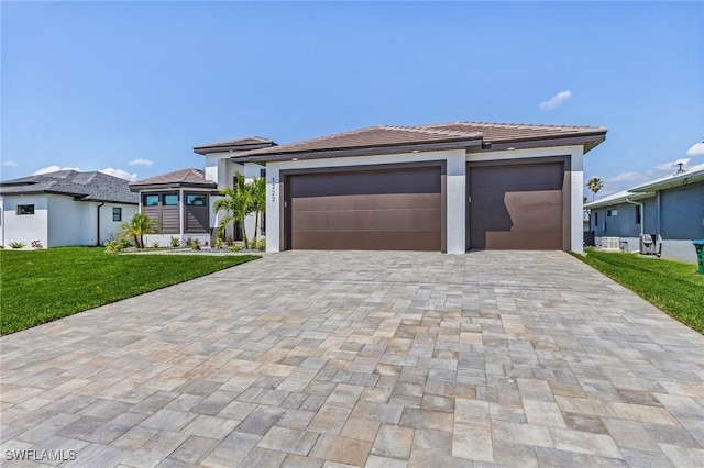 prairie-style home featuring a front lawn, decorative driveway, a garage, and stucco siding