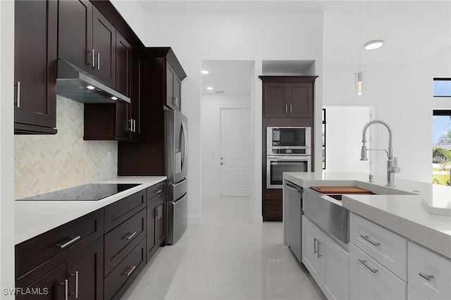 kitchen with a sink, hanging light fixtures, under cabinet range hood, appliances with stainless steel finishes, and tasteful backsplash