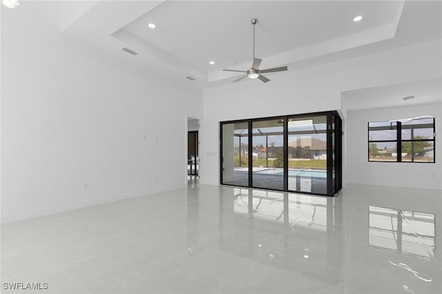 empty room featuring a tray ceiling, plenty of natural light, baseboards, and visible vents