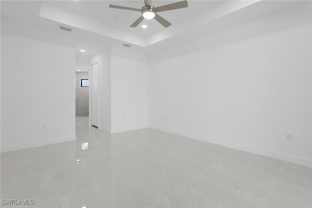 empty room with baseboards, visible vents, a ceiling fan, and a tray ceiling