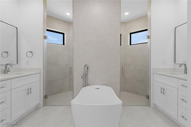 bathroom featuring a shower stall, a freestanding tub, two vanities, and a sink