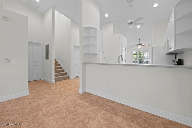 kitchen with a towering ceiling, built in shelves, sink, electric panel, and white cabinetry