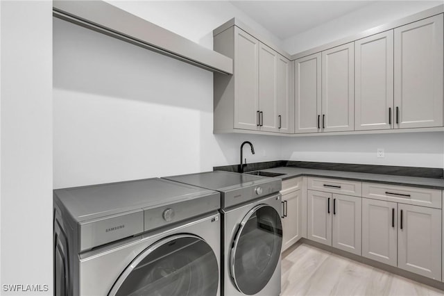 clothes washing area featuring washer and clothes dryer, cabinets, light wood-type flooring, and sink