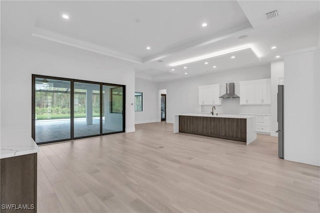 kitchen with stainless steel fridge, wall chimney exhaust hood, sink, a large island with sink, and white cabinetry