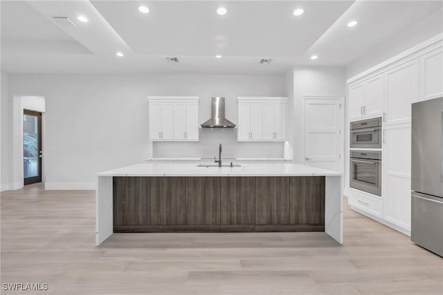 kitchen featuring sink, wall chimney exhaust hood, stainless steel fridge, a spacious island, and white cabinets