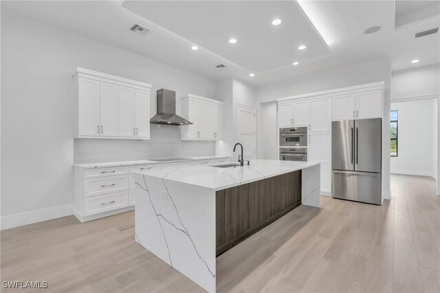 kitchen with stainless steel appliances, a spacious island, sink, wall chimney range hood, and white cabinetry