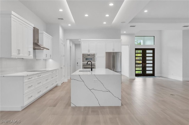 kitchen featuring sink, wall chimney exhaust hood, a large island, white cabinetry, and stainless steel appliances