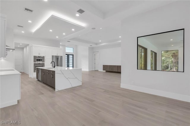 kitchen featuring light stone countertops, sink, stainless steel appliances, a center island with sink, and white cabinets