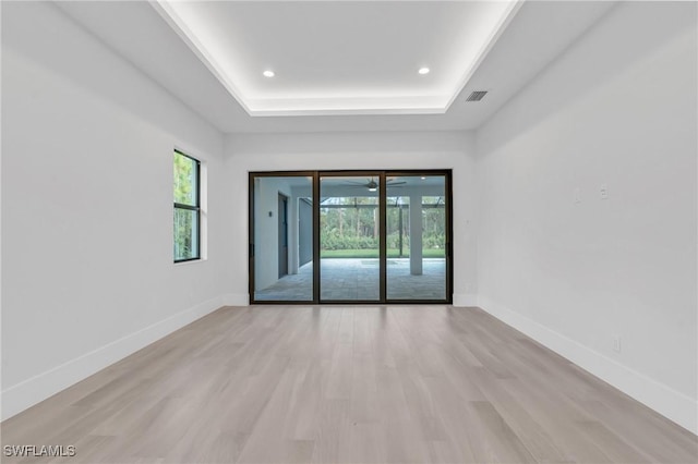 spare room featuring light wood-type flooring and a tray ceiling