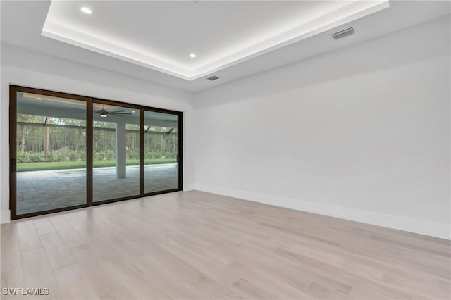 unfurnished room featuring a raised ceiling, light hardwood / wood-style flooring, and ceiling fan