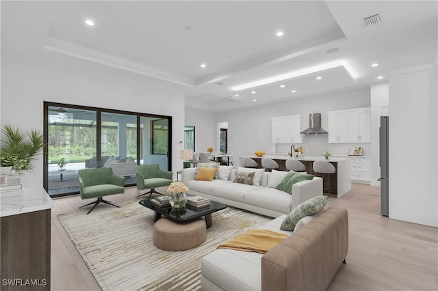 living room with a raised ceiling, sink, and light hardwood / wood-style flooring