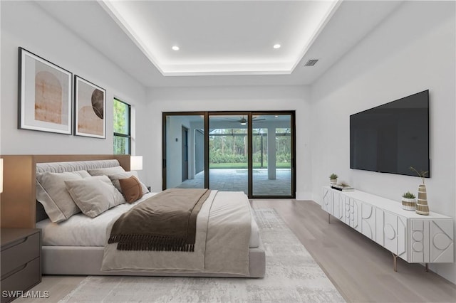 bedroom featuring a raised ceiling, access to exterior, and light wood-type flooring