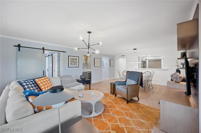 living room featuring a barn door, an inviting chandelier, light hardwood / wood-style flooring, and crown molding