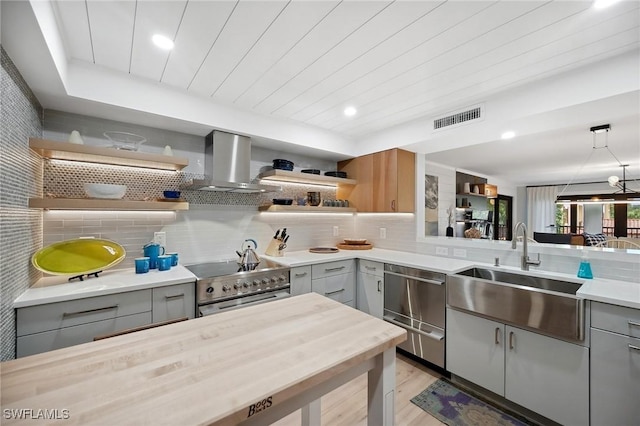 kitchen with sink, wall chimney exhaust hood, hanging light fixtures, gray cabinets, and appliances with stainless steel finishes