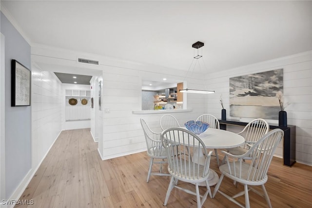 dining room featuring wooden walls, light hardwood / wood-style flooring, and ornamental molding