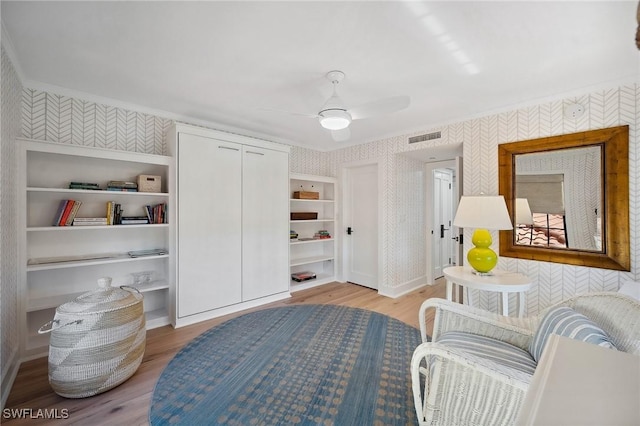 living area featuring ceiling fan, light hardwood / wood-style floors, ornamental molding, and built in shelves