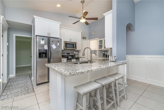 kitchen with sink, light tile patterned floors, light stone counters, white cabinets, and appliances with stainless steel finishes