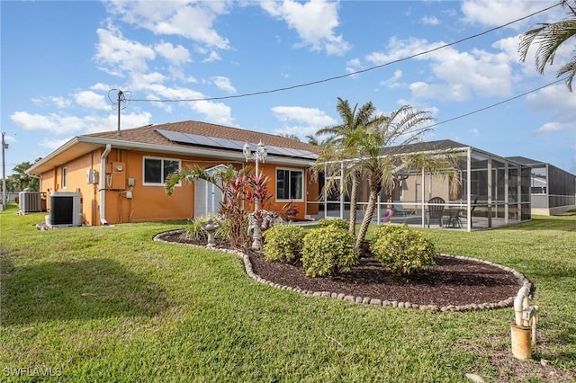 rear view of property with a lanai, central AC, a lawn, and solar panels