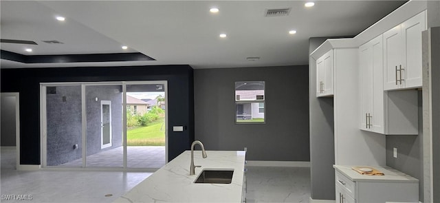 kitchen featuring white cabinets, a tray ceiling, light stone counters, and sink