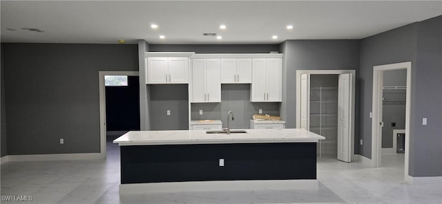 kitchen with light stone countertops, a center island with sink, white cabinetry, and sink