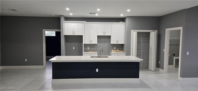 kitchen with white cabinets, light stone counters, and a kitchen island with sink