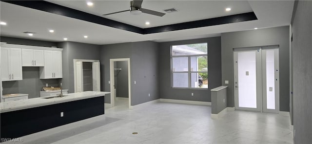 kitchen with white cabinets, a tray ceiling, light stone counters, and ceiling fan