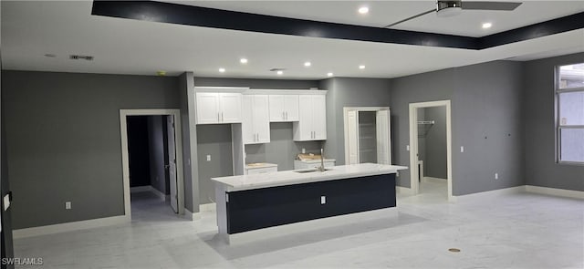 kitchen featuring white cabinetry, sink, ceiling fan, light stone counters, and an island with sink