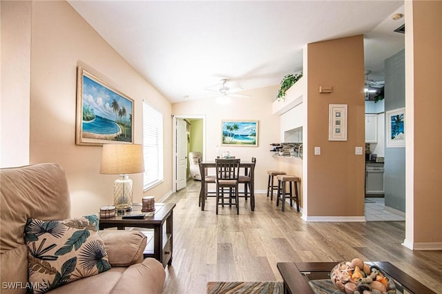 living room with ceiling fan, light hardwood / wood-style floors, and vaulted ceiling