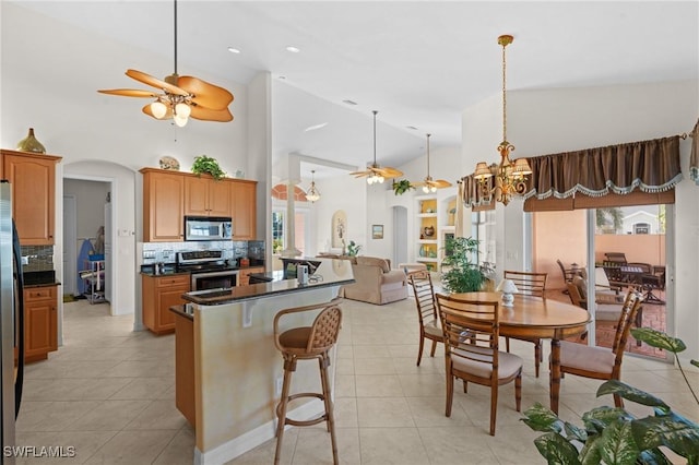 kitchen featuring tasteful backsplash, a breakfast bar, light tile patterned flooring, ceiling fan with notable chandelier, and appliances with stainless steel finishes