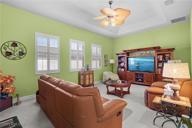 carpeted living room with a raised ceiling and ceiling fan