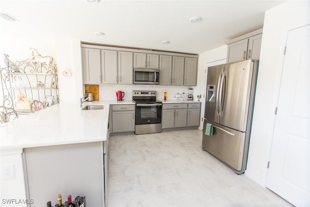 kitchen with stainless steel appliances, gray cabinets, sink, and kitchen peninsula