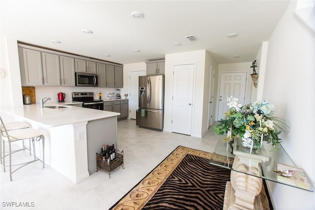 kitchen with sink, a breakfast bar area, appliances with stainless steel finishes, gray cabinets, and kitchen peninsula