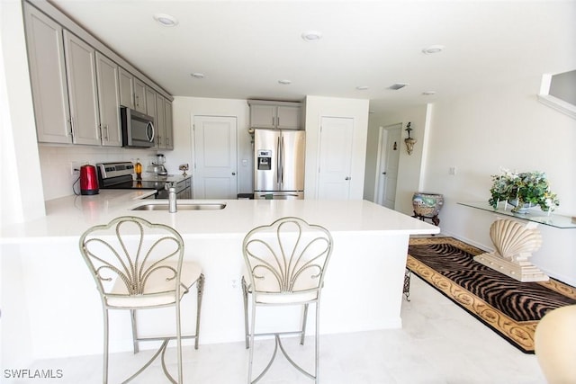 kitchen featuring gray cabinets, a breakfast bar area, backsplash, kitchen peninsula, and stainless steel appliances