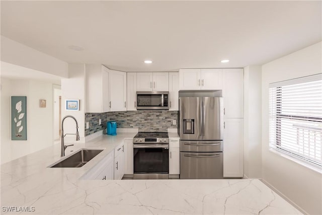 kitchen featuring decorative backsplash, light stone counters, stainless steel appliances, sink, and white cabinets