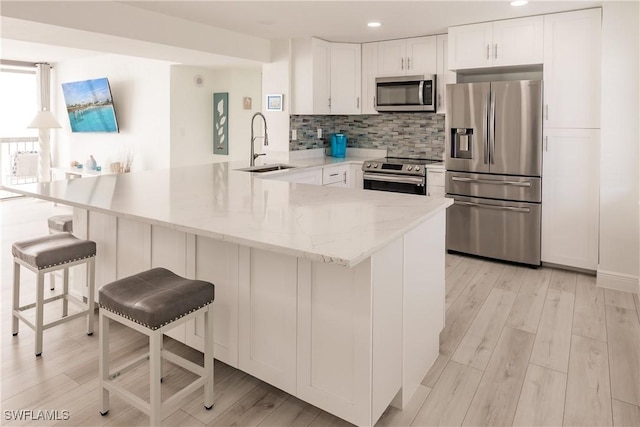 kitchen featuring sink, appliances with stainless steel finishes, white cabinetry, a kitchen bar, and kitchen peninsula