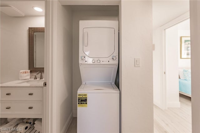 laundry room with stacked washer / drying machine, sink, and light wood-type flooring