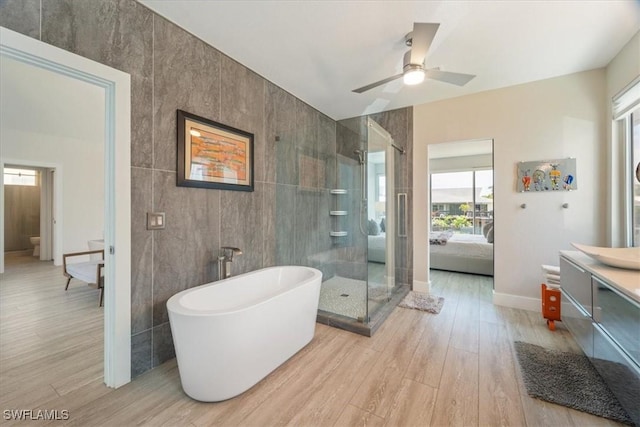 bathroom featuring vanity, plus walk in shower, ceiling fan, tile walls, and wood-type flooring