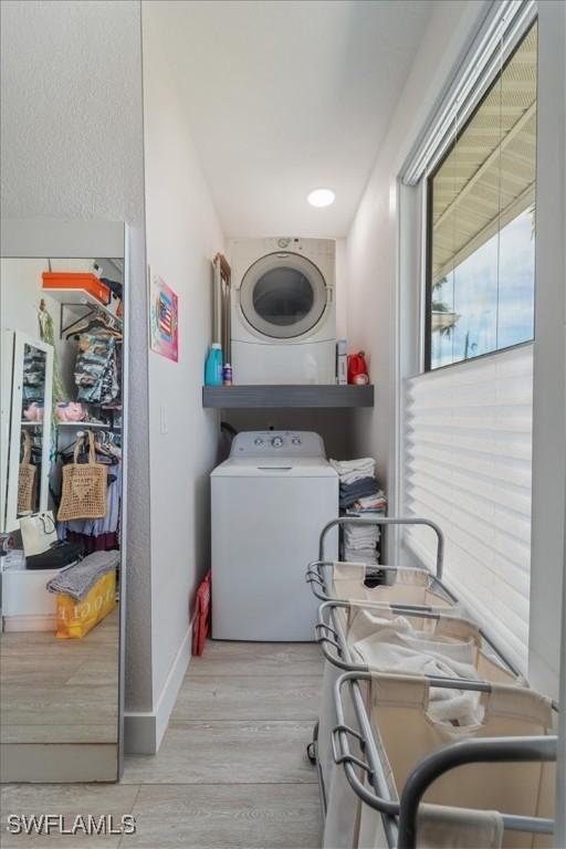 washroom with stacked washing maching and dryer and light hardwood / wood-style floors