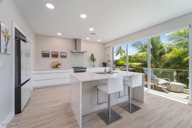 kitchen featuring freestanding refrigerator, stainless steel stove, modern cabinets, wall chimney range hood, and a sink